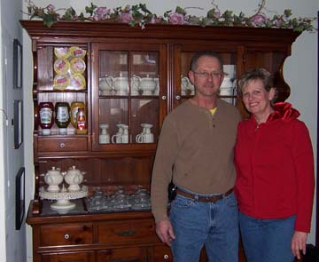 Norm and Sandy Gerber stand in front of the breakfront holding pretty teapots and cups.